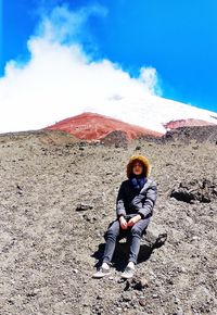 Full length of teenage boy sitting on mountain against sky