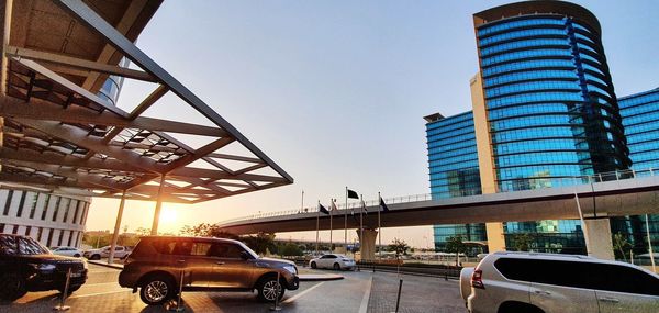 Cars on road by buildings against sky during sunset