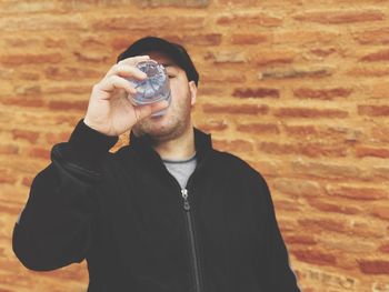 Man drinking water from bottle against brick wall