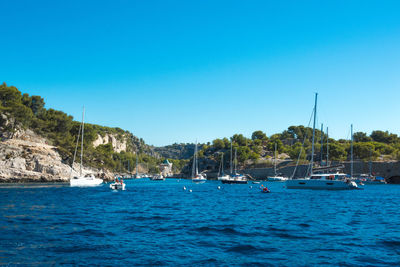 Boats moored on sea against clear blue sky