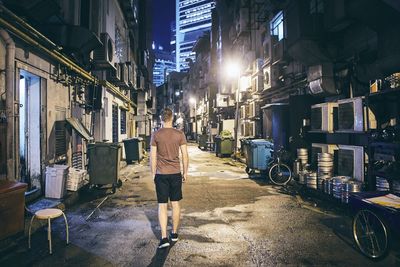 Rear view of man walking in alley at illuminated city during night