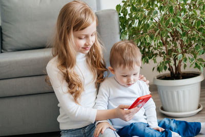 Girl with a baby brother sitting on the floor with a smartphone