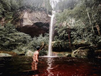 Full length of shirtless man splashing water in forest