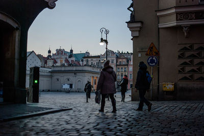 Rear view of people walking on footpath by buildings