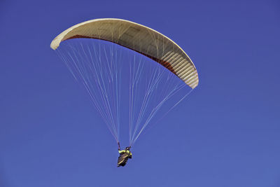 Low angle view of person paragliding against clear blue sky on sunny day