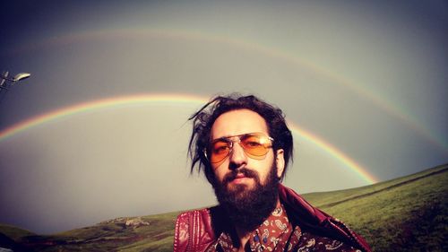 Portrait of smiling young man against rainbow in sky