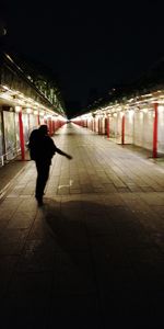 Rear view of man walking on illuminated street at night