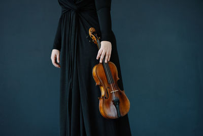 Midsection of woman holding violin against blue background