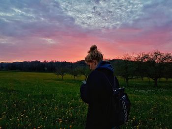 Rear view of woman on field against sky during sunset