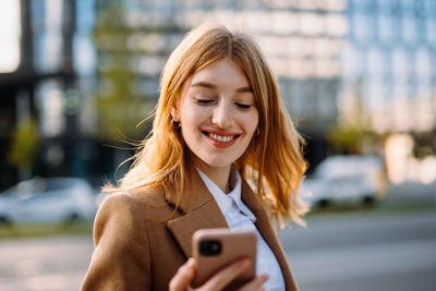 A woman is smiling while looking at her cell phone