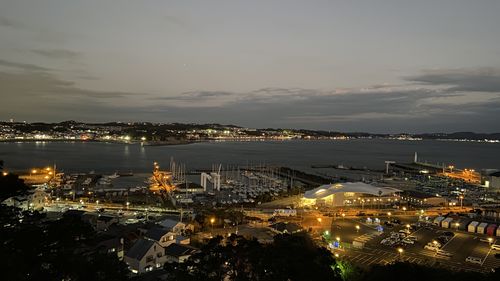 High angle view of illuminated city by sea against sky