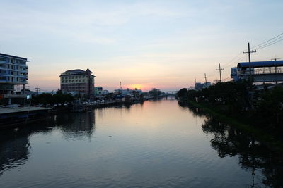 Scenic view of river by buildings against sky during sunset