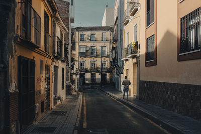 Rear view of man walking on footpath amidst buildings