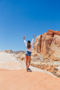 Full length of woman jumping on sand at desert against clear blue sky