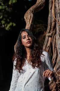 Portrait of woman standing by tree trunk