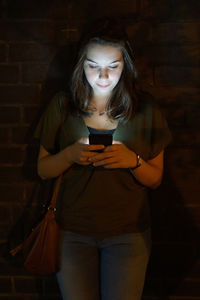 Beautiful woman text messaging against brick wall at night