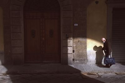 Full length of man sitting on footpath against building