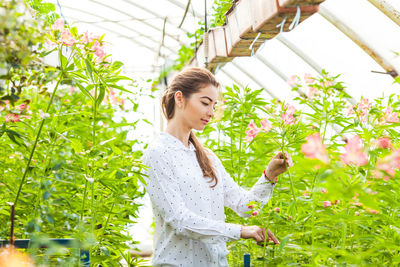 Woman standing by plants in greenhouse