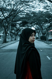 Portrait of woman standing by road against trees