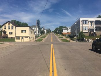 Empty road amidst buildings against sky on sunny day