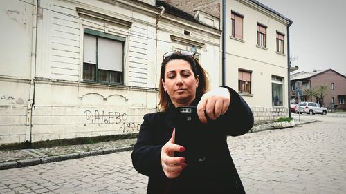 Mature woman taking selfie while standing on footpath against buildings