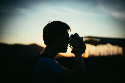 Young man photographing against sky during sunset