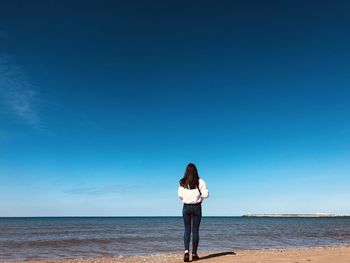 Rear view of woman walking at beach against blue sky