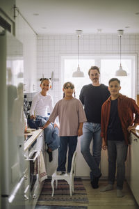 Portrait of gay couple with daughters standing in kitchen at home