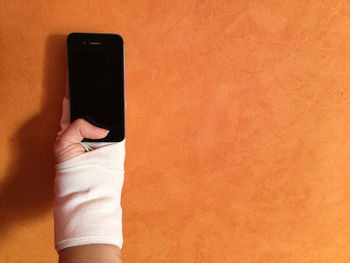 Close-up of human hand holding mobile phone against wall