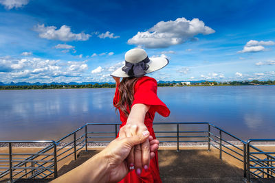Cropped image of man holding woman hand while looking at lake