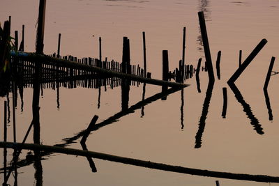 Wooden posts in lake against sky during sunset