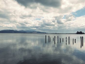 Wooden posts in sea against sky
