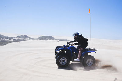 Full length of young man riding quadbike at pismo beach against clear sky during sunny day
