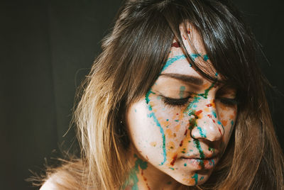 Close-up of woman with paint on face against black background