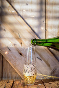 Close-up of bottle pouring champagne in glass on wooden table