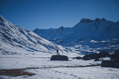 Man standing on rock on snow covered land against mountains and clear sky
