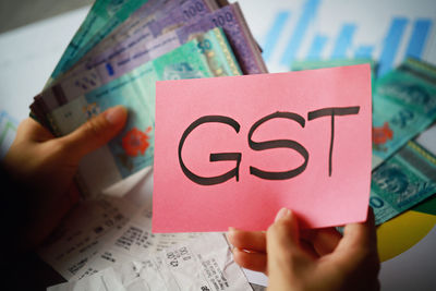 Cropped image of woman holding currency with gst text on paper