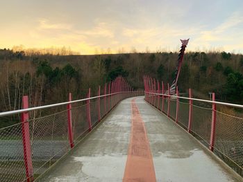 Footpath by fence against sky during sunset