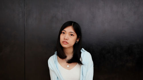 Portrait of beautiful young woman standing against wall