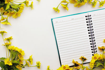 High angle view of blank spiral notepad amidst yellow flowers on table