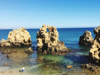 Scenic view of rocks in sea against clear blue sky