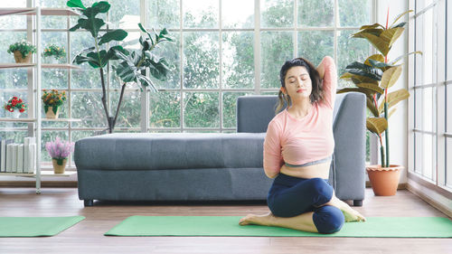 Full length of woman sitting on potted plant at home