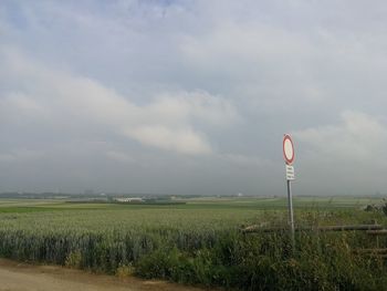 Road sign on field against sky