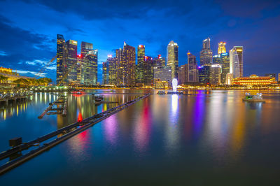 Illuminated buildings by river against sky at night