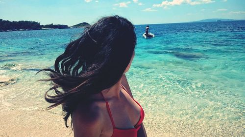 Young woman in bikini looking at her friend on boat in sea at beach during sunny day