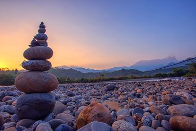 Stack of stones on beach against sky during sunset