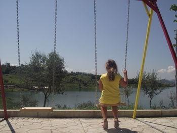 Rear view of woman on swing at playground against sky