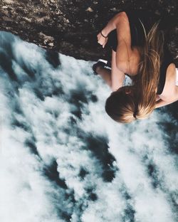 Upside down image of woman sitting on rock formation against cloudy sky