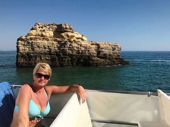 Portrait of mature woman wearing bikini while sitting in yacht sailing on sea