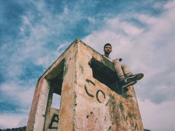 Low angle view of man sitting on abandoned building